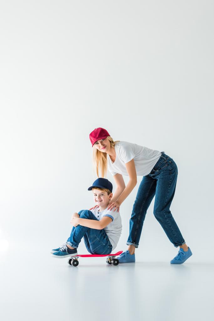 щаслива мати в червоній шапці штовхає сина на ковзанах на білому
 - Фото, зображення