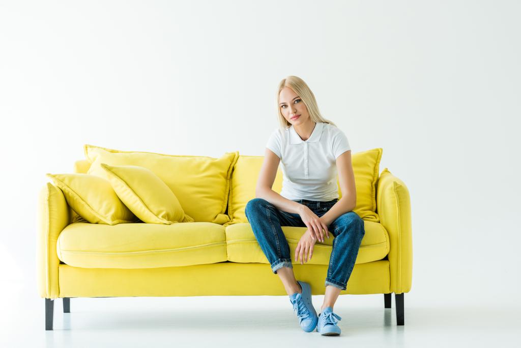 vonzó nő, sárga kanapén ül és nézi a fényképezőgép fehér - Fotó, kép