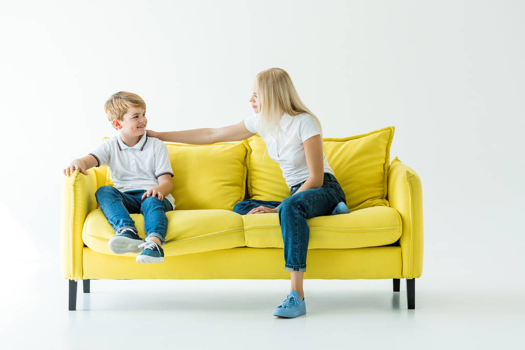 moeder en zoon op gele sofa zitten en kijken naar elkaar op wit - Foto, afbeelding