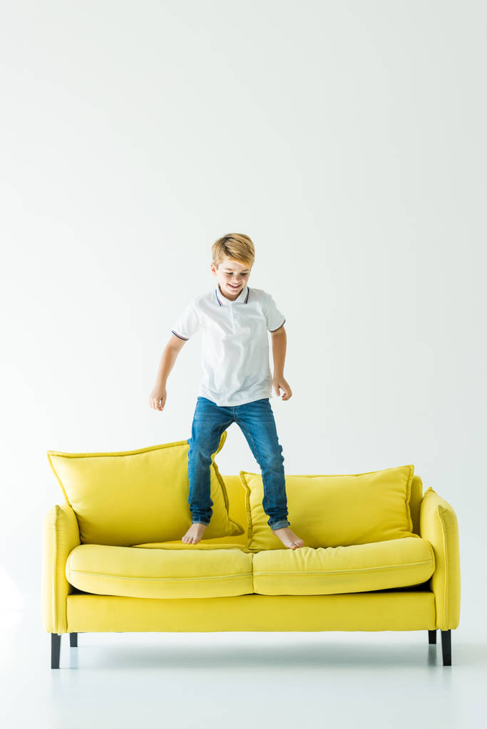 felice adorabile ragazzo che salta sul divano giallo su bianco
 - Foto, immagini