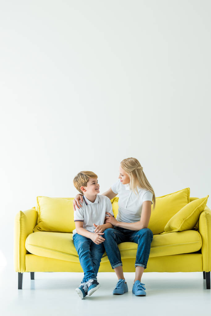 moeder van knuffelen gelukkige zoon op gele sofa op wit - Foto, afbeelding