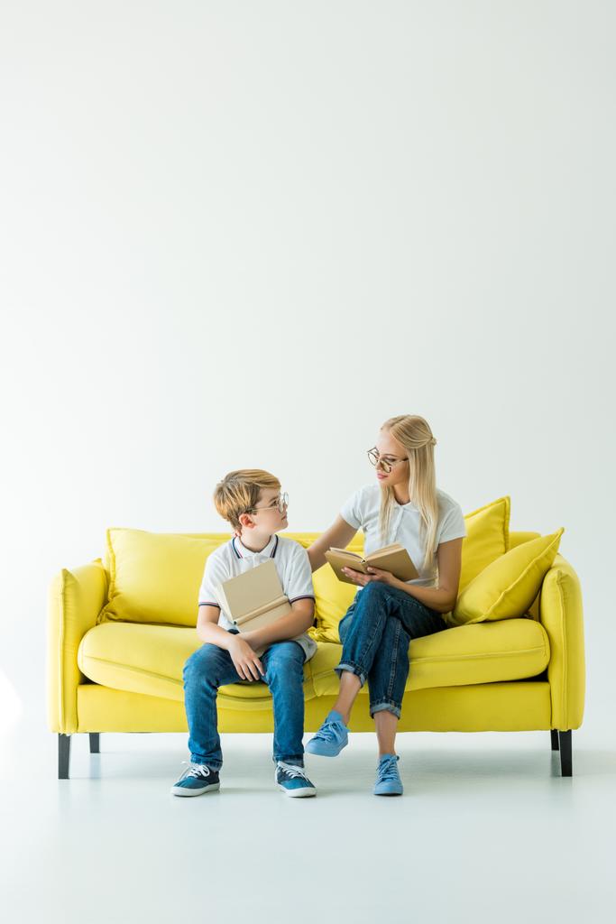 moeder en zoon houden van boeken en kijken elkaar op gele Bank - Foto, afbeelding