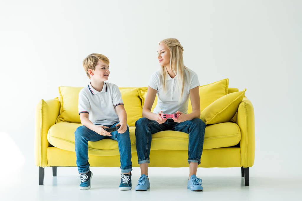 madre e figlio che giocano al videogioco e si guardano sul divano giallo sul bianco
 - Foto, immagini