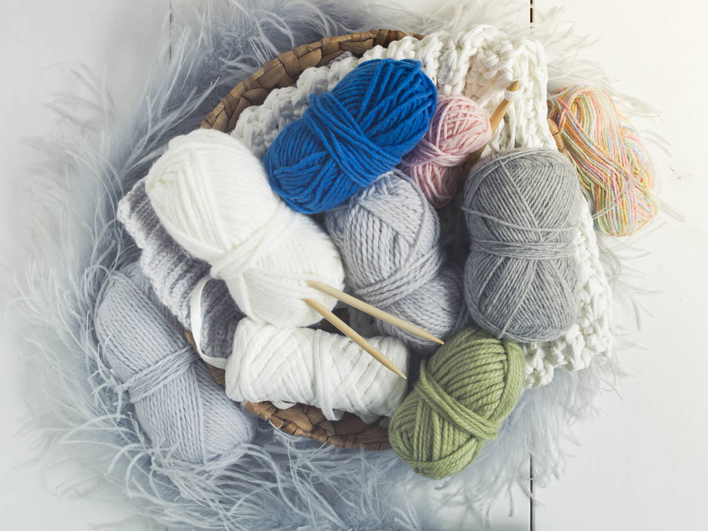 Diferentes tipos de lana de colores en la cesta de mimbre en el suelo blanco
 - Foto, Imagen