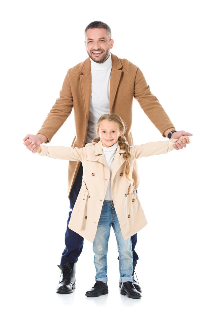 πατέρας και κόρη, κρατώντας τα χέρια και θέτοντας σε μπεζ παλτό, απομονώνονται σε λευκό - Φωτογραφία, εικόνα