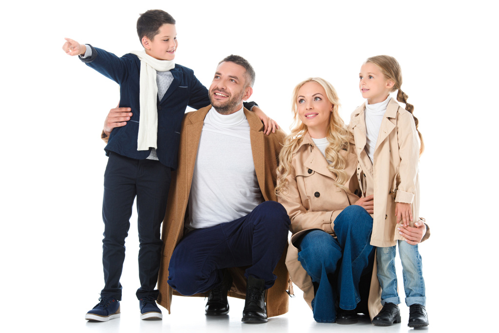 stylische glückliche Familie, die sich mit Kindern in beigen Mänteln umarmt, Junge zeigt etwas Isoliertes auf weißem Grund - Foto, Bild