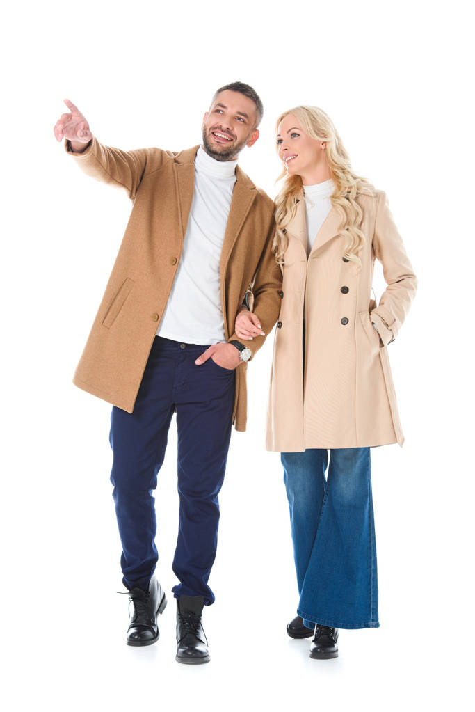 happy stylish couple posing in trendy autumn coats, man showing something isolated on white - Photo, Image