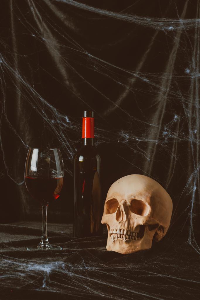 Gruseliger Totenkopf und Rotwein auf schwarzem Tuch mit Spinnennetz - Foto, Bild