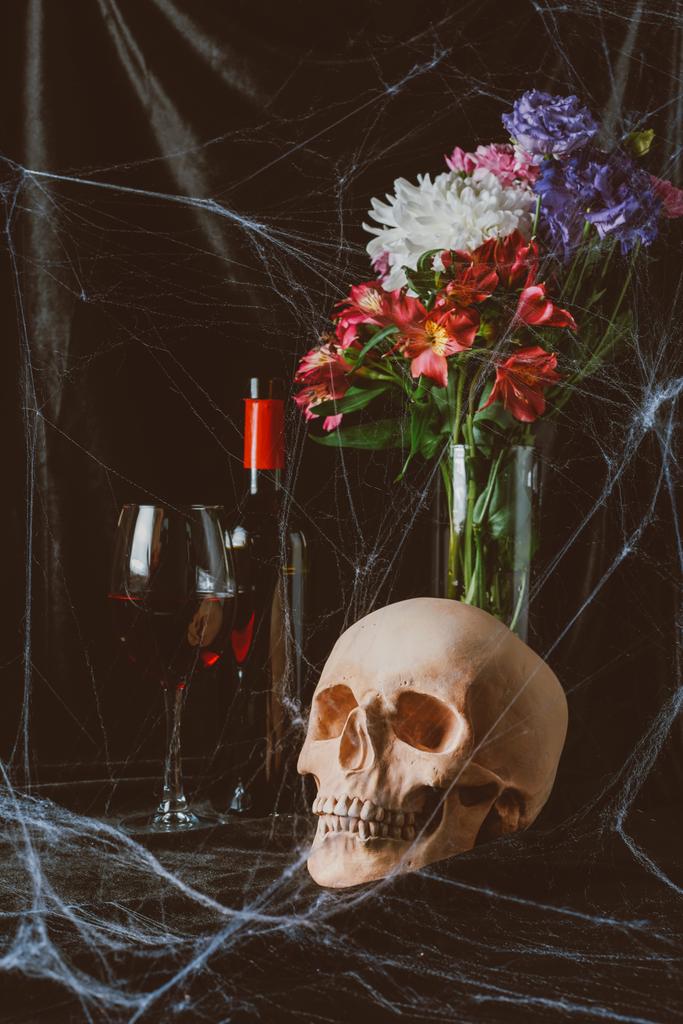 Halloween Totenkopf, Rotwein und Vase mit Blumen auf schwarzem Tuch mit Spinnennetz - Foto, Bild
