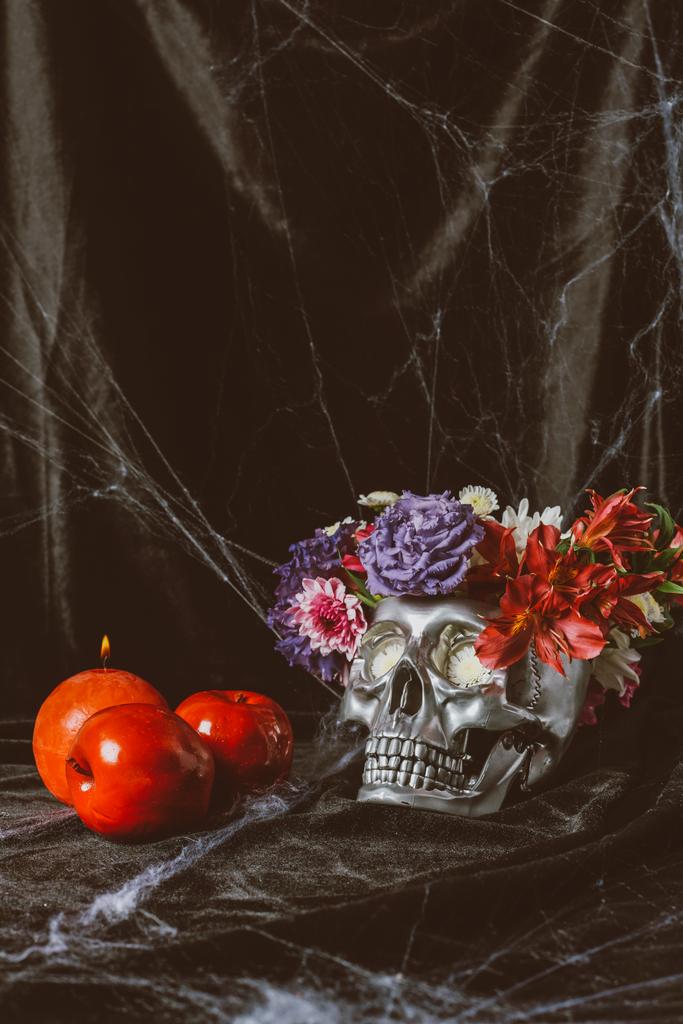 срібний череп з квітами, свічкою та яблуками на чорній тканині з павутиною
  - Фото, зображення