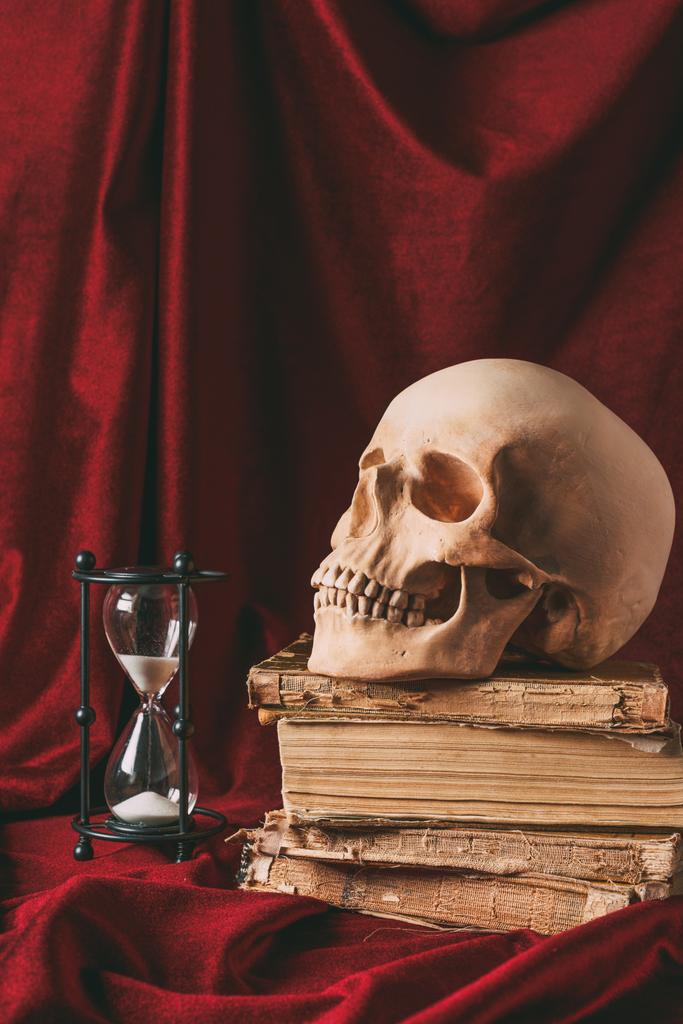 Halloween schedel op oude boeken met zandloper op rode doek - Foto, afbeelding