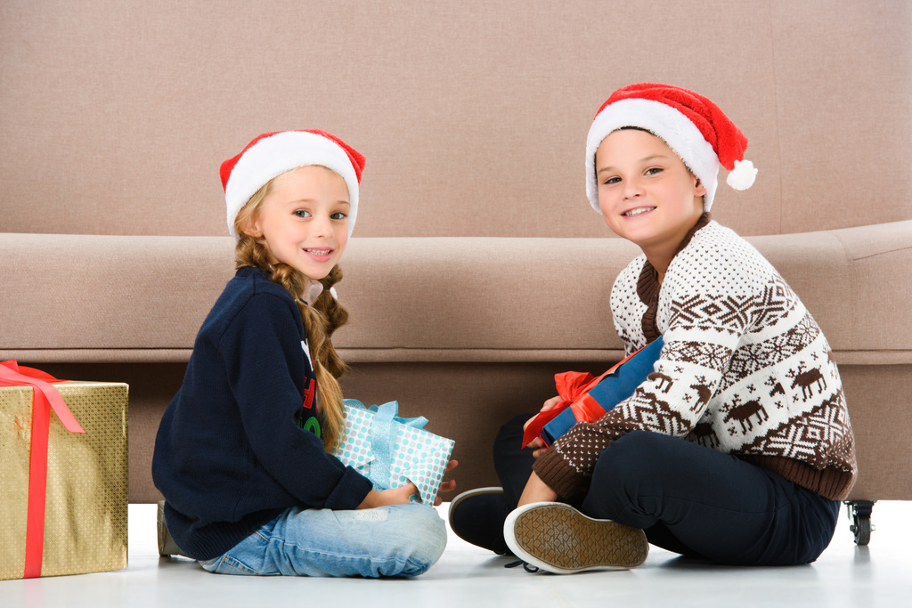 Noel Baba şapkası kanepe Noel hediyeleri ile oturan çocuklarda - Fotoğraf, Görsel