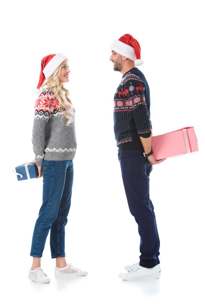 Χριστούγεννα ζευγάρι σε μπλούζες και καπέλα santa κρύβονται κουτιά δώρων, απομονώνονται σε λευκό - Φωτογραφία, εικόνα