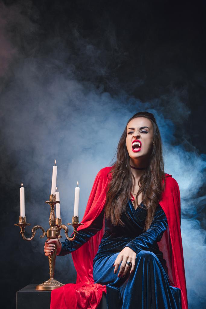donna in costume da vampiro in possesso di candelabro vintage sul buio con il fumo
  - Foto, immagini
