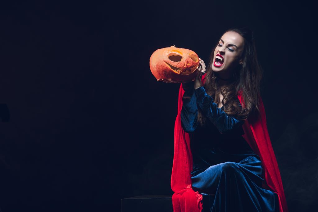 mysterie vrouw in vampier kostuum jack o lantern op donkere achtergrond te houden - Foto, afbeelding