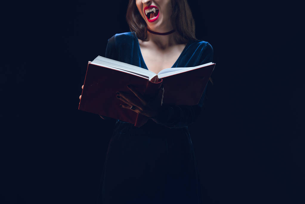 Vista ritagliata di donna vampiro in possesso di libro magico isolato su nero
 - Foto, immagini
