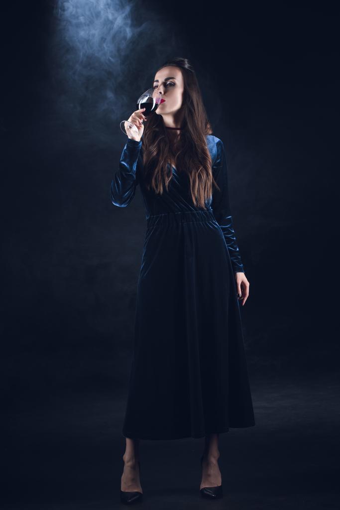 vampire woman drinking blood from wineglass on dark background with smoke  - Photo, Image