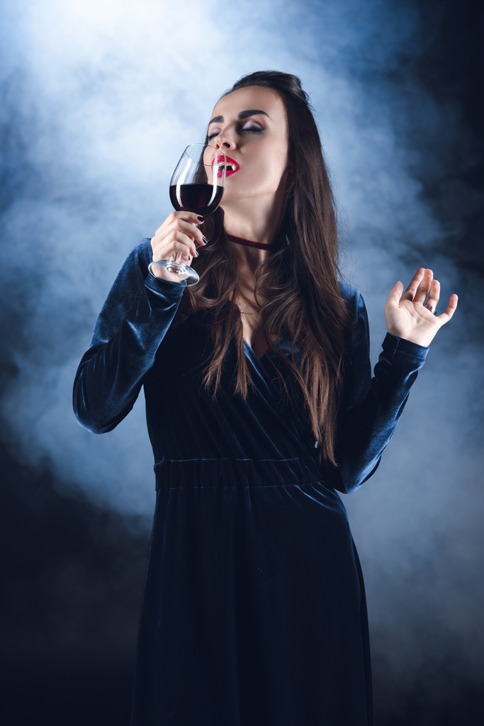 vampire drinking blood from wineglass on dark background with smoke  - Photo, Image