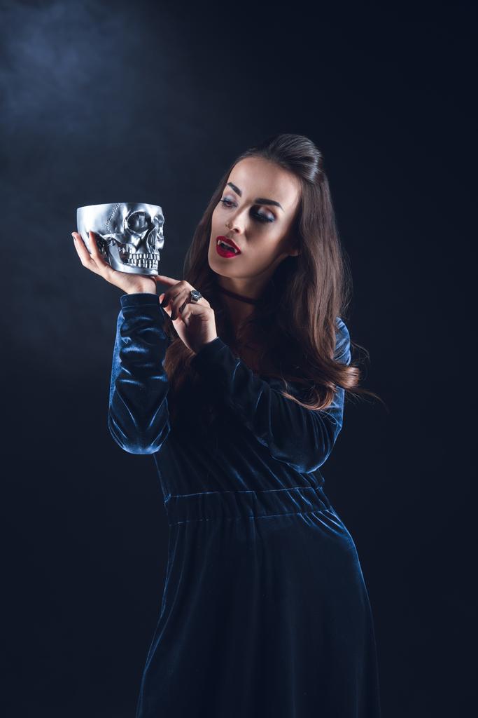 Vampire nő tartja fém koponya sötét háttér, füst  - Fotó, kép