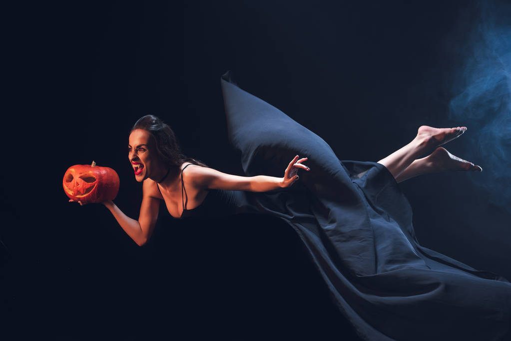 vrouw in vampier kostuum holding hefboom o lantaarn en vliegen op duisternis met rook  - Foto, afbeelding