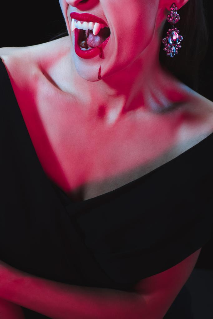 Ausgeschnittene Ansicht einer Vampirfrau, die ihre Vampirzähne auf dunklem Hintergrund zeigt - Foto, Bild