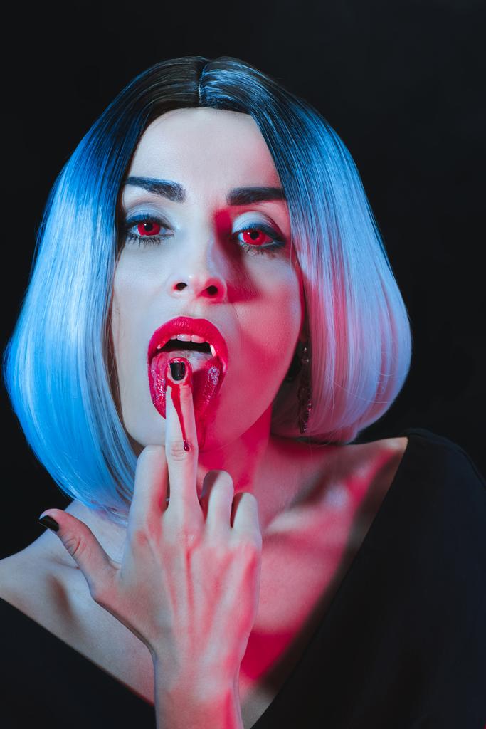 sexy vampire licking her middle finger isolated on black - Photo, Image