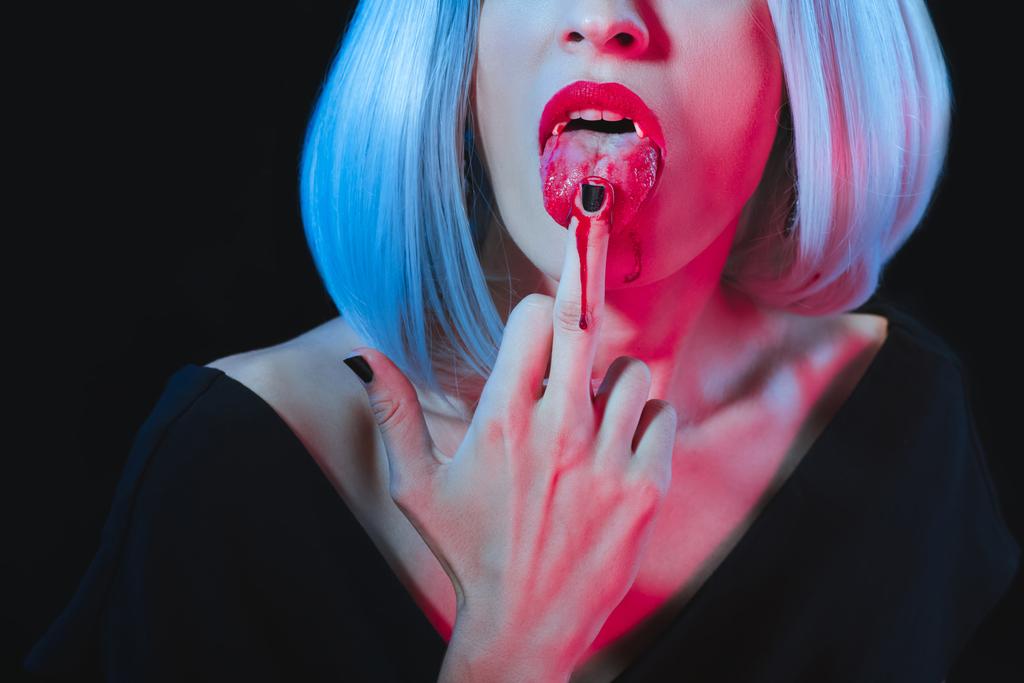 recortado vista de vampiro mujer lamiendo su dedo medio aislado en negro
 - Foto, imagen
