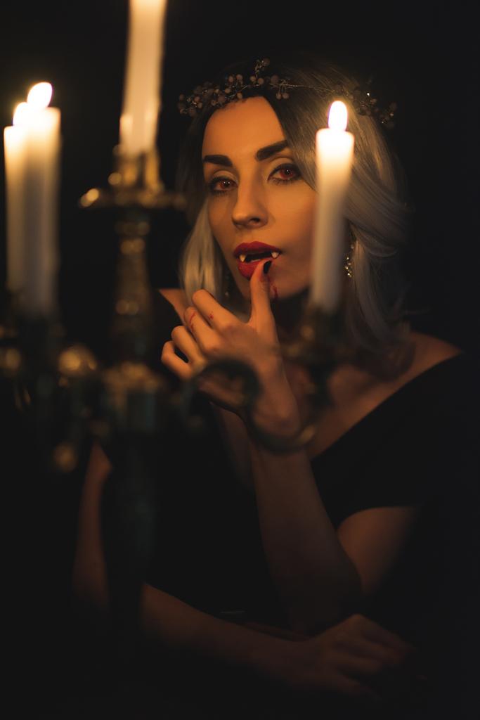 Frau im Vampirkostüm leckt ihre Finger mit Leuchter im Vordergrund  - Foto, Bild