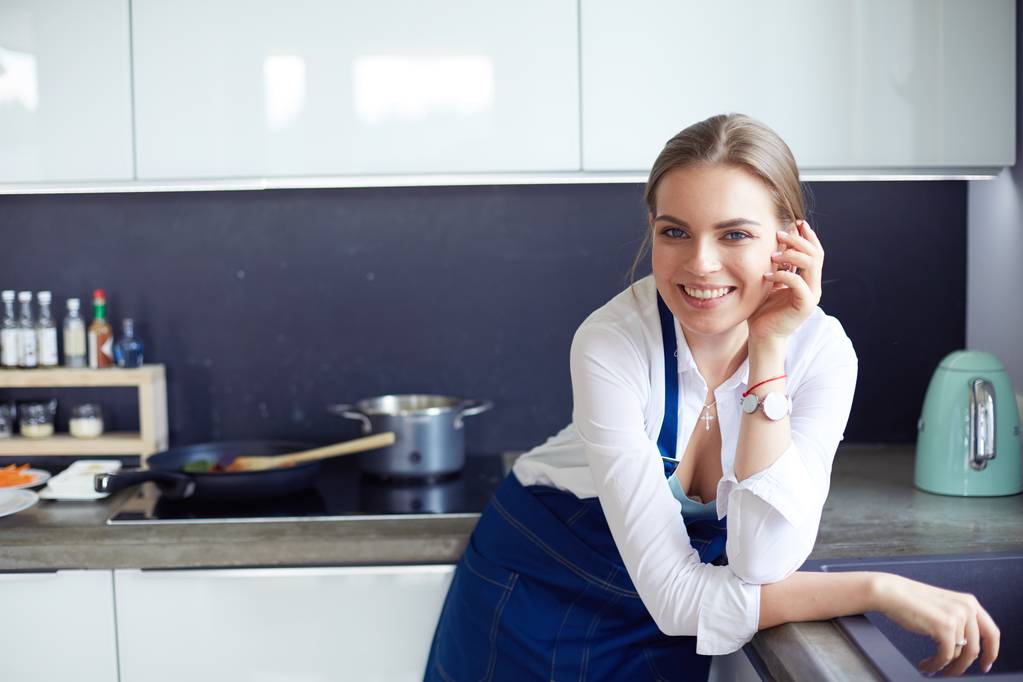 Kollarını mutfak arka planında kavuşturmuş genç bir kadının portresi. - Fotoğraf, Görsel