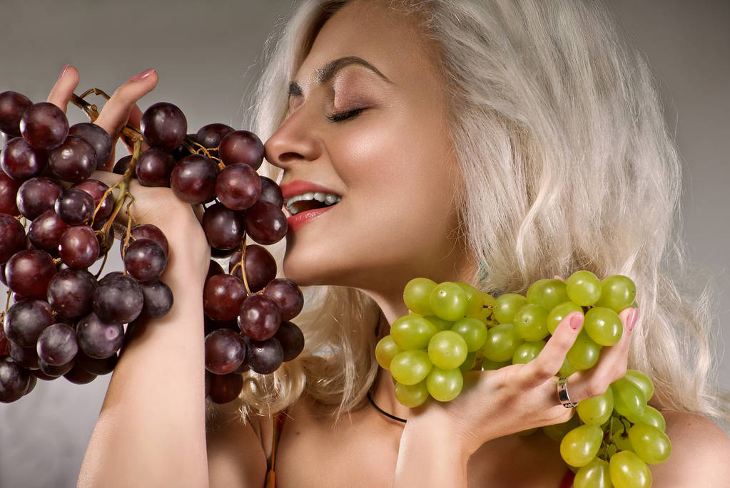 young, pretty blonde with grapes on a photo studio. natural makeup. - Photo, Image