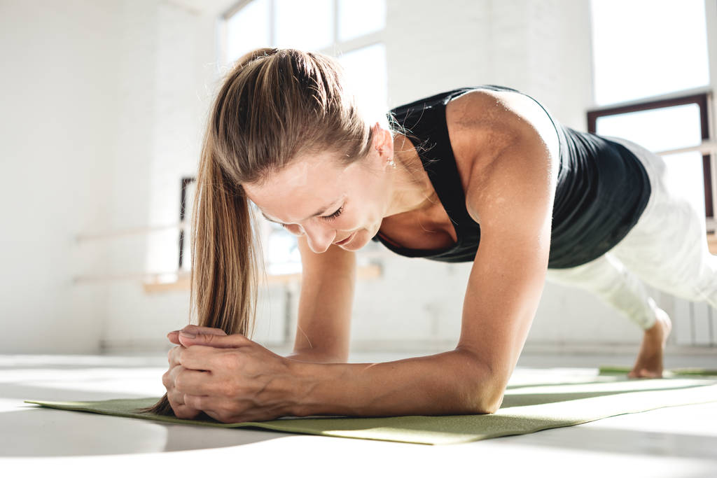 Sportos erős nő csinál crossfit edzés jóga matracot a napsütötte gumi. Fiatal izmos nő core gyakorlása, fitness szőnyeg, fehér edzőteremben csinál - Fotó, kép
