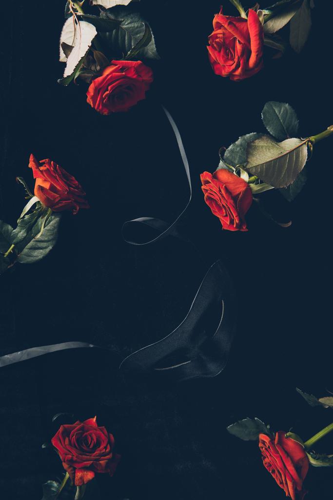 von oben mit schwarzer Maske und schönen roten Rosen auf schwarz - Foto, Bild