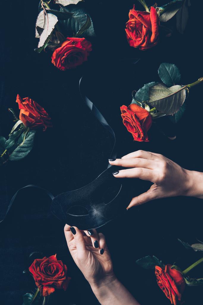 recortado disparo de mujer sosteniendo máscara negra y hermosas rosas rojas en negro
 - Foto, Imagen