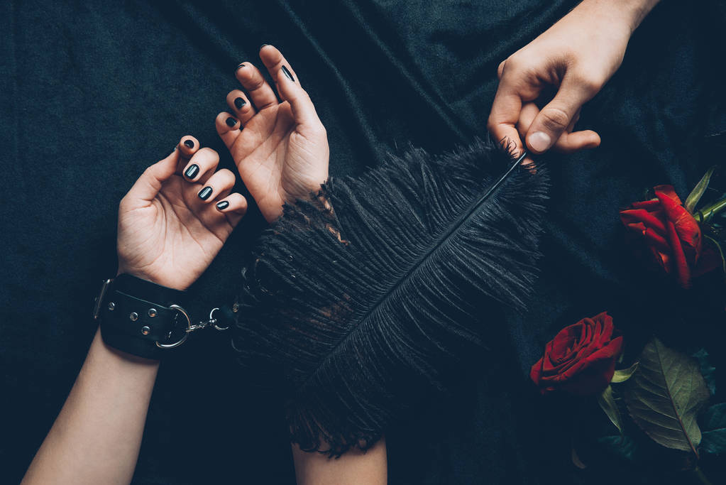 ritagliato colpo di uomo in possesso di piuma nera e donna in manette di pelle
 - Foto, immagini