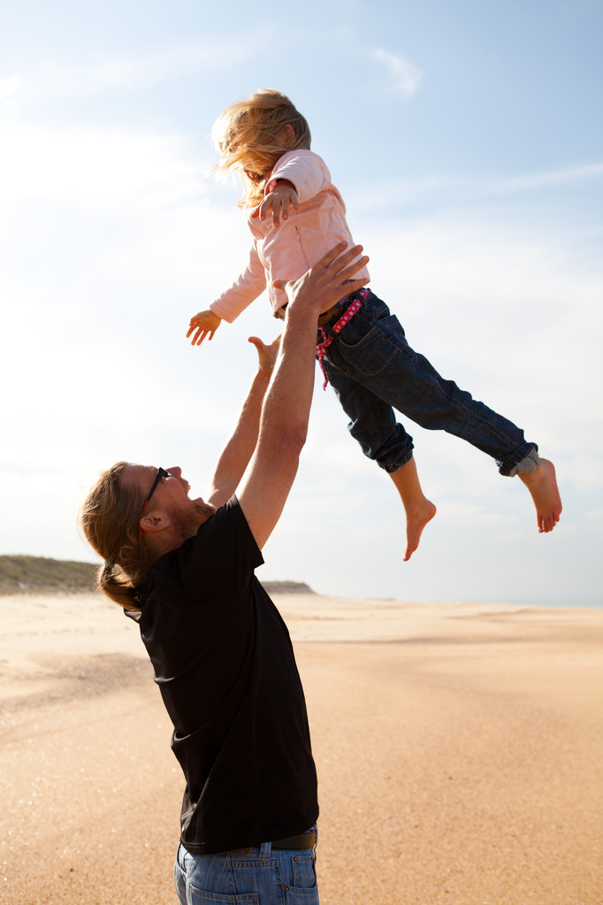 Батько кидає дочку в повітря на пляжі
 - Фото, зображення