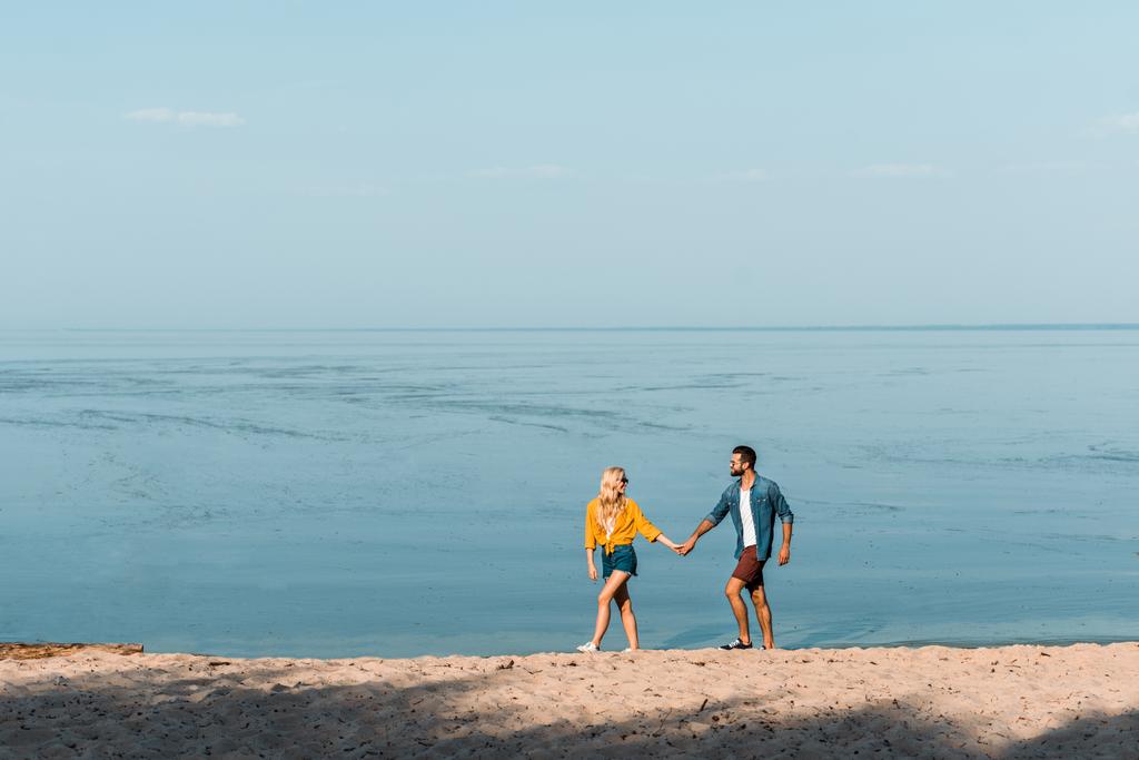 Paar hält Händchen und geht am Strand spazieren  - Foto, Bild