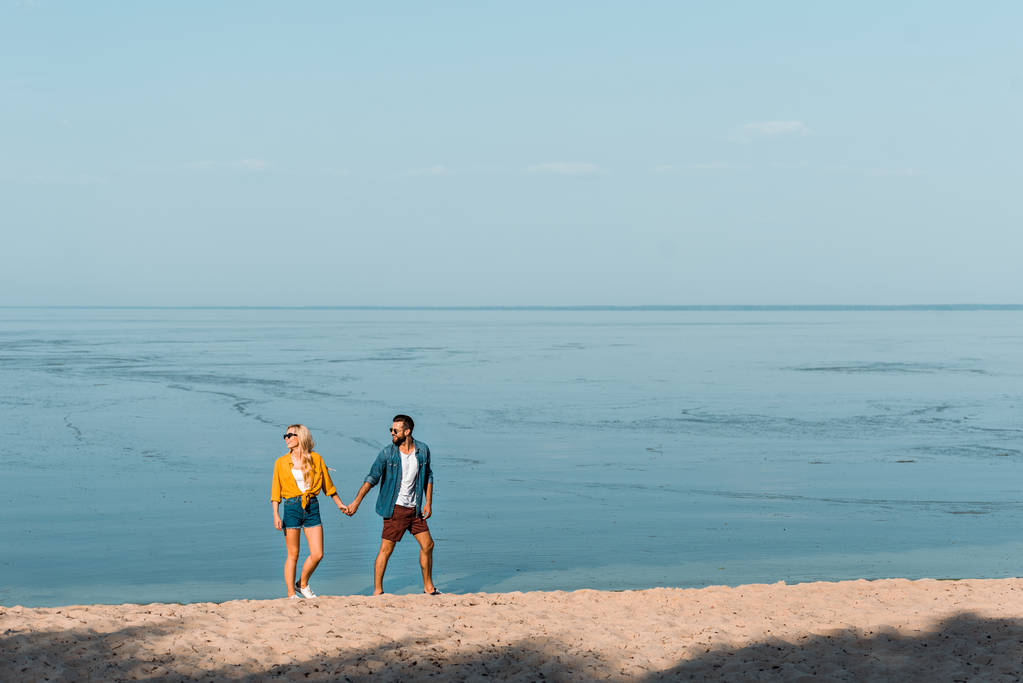 casal de mãos dadas e caminhando na praia de areia
 - Foto, Imagem