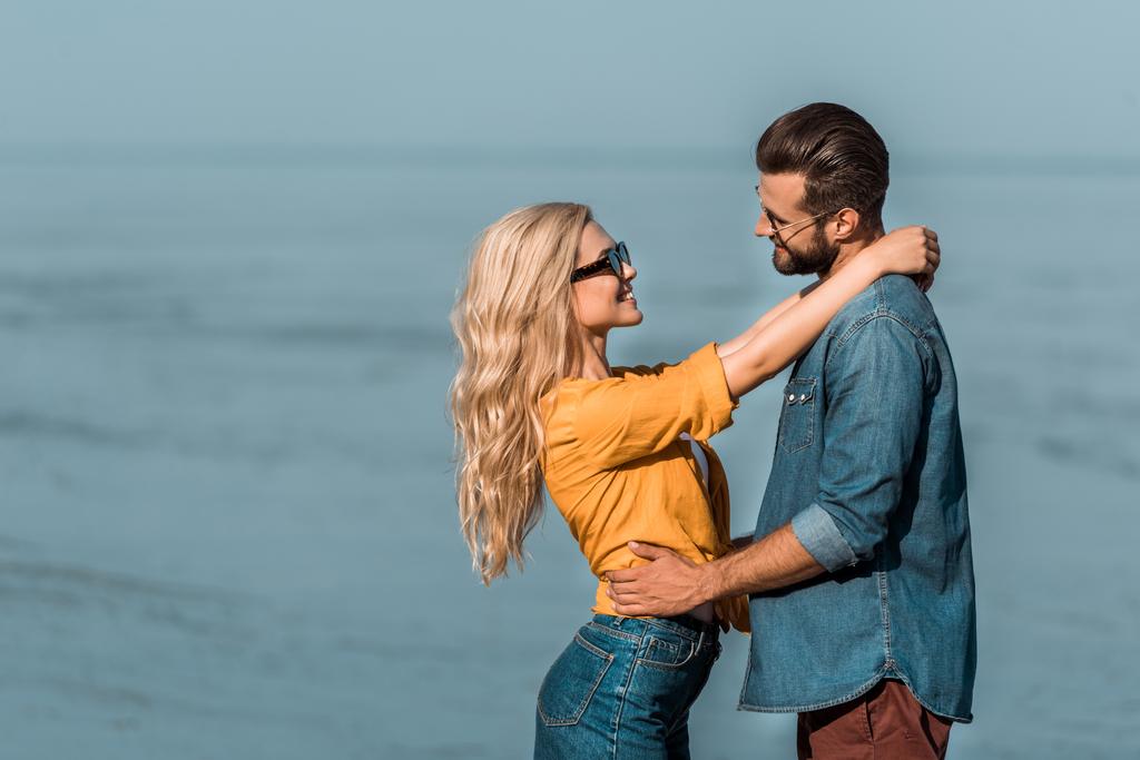 couple en lunettes de soleil câlins et regarder l'autre près de l'océan
 - Photo, image