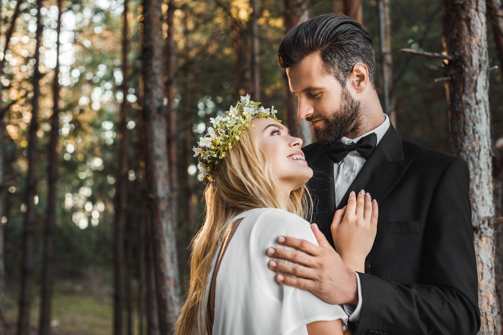 bella sposa in abito bianco e bello sposo in abito abbracciarsi nella foresta e guardarsi l'un l'altro
 - Foto, immagini