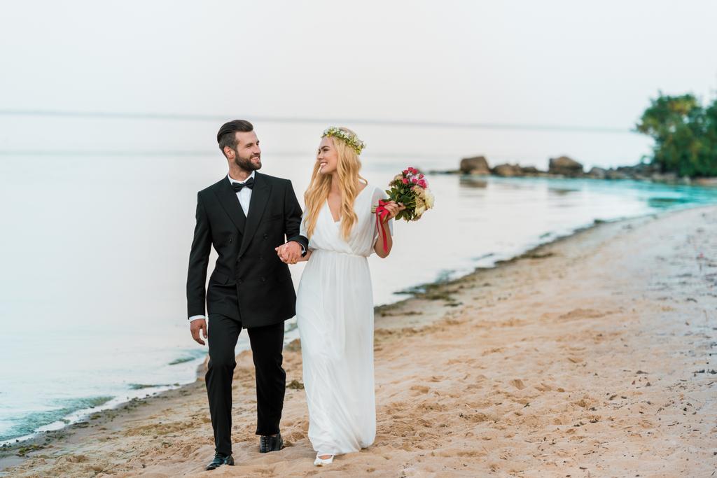 Svatební pár držení rukou a chůzi na písčité mořské pláži - Fotografie, Obrázek