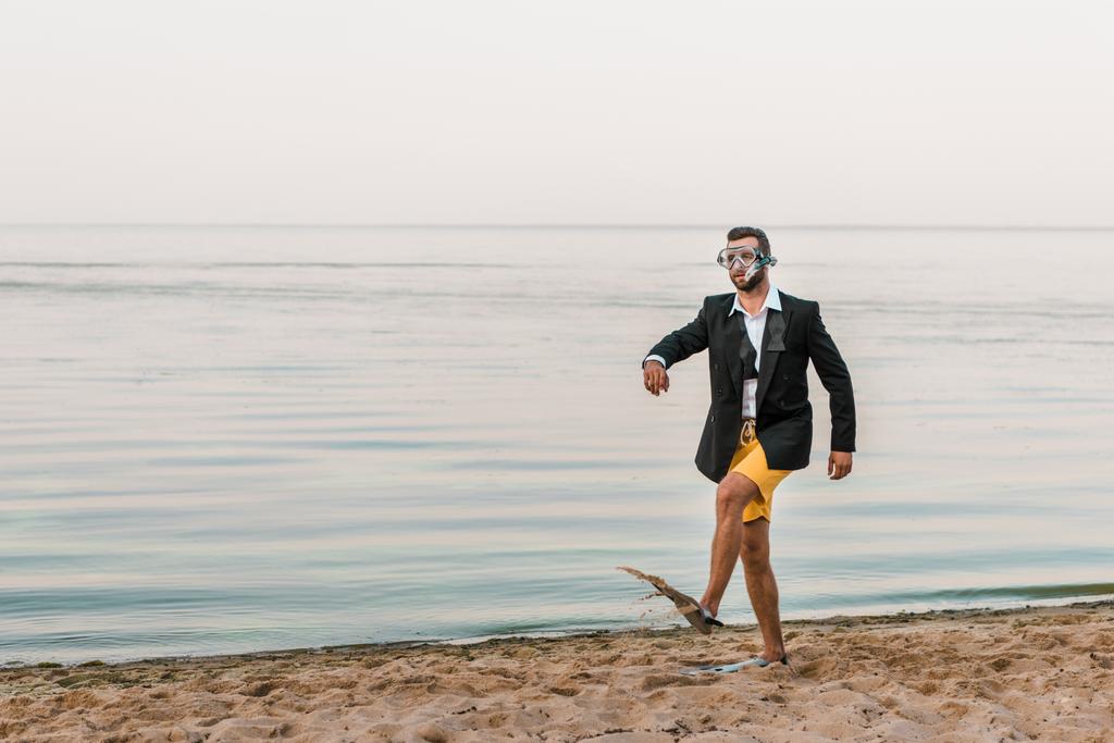 adam siyah ceket ve maske ve palet deniz kıyısında yüzme ile yürüyüş şort - Fotoğraf, Görsel