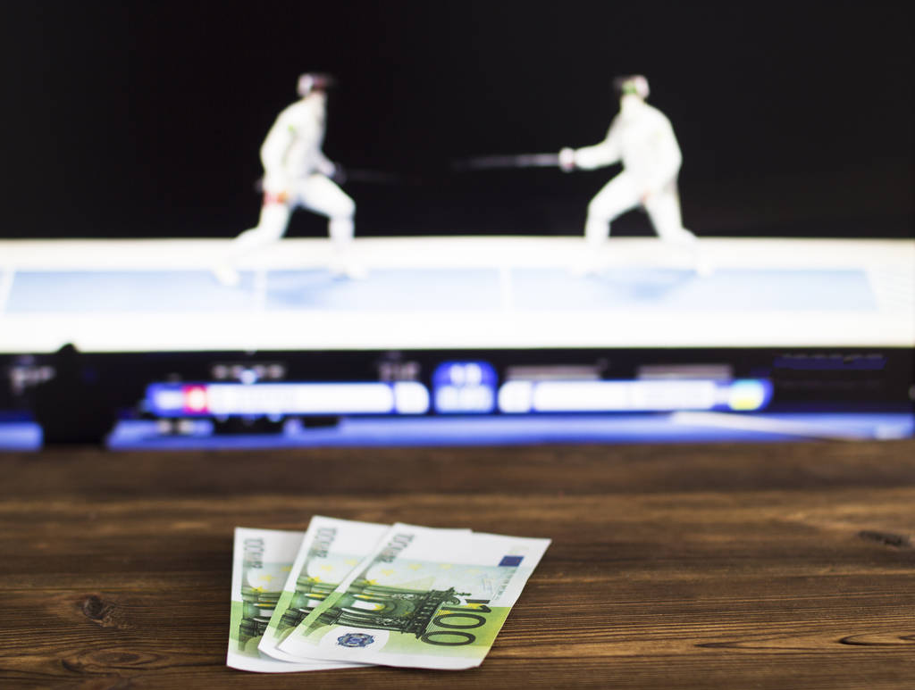Euro-Geld auf dem Hintergrund eines Fernsehers, auf dem Sportfechten, Sportwetten, Schwertkampf, Euro zu sehen sind - Foto, Bild