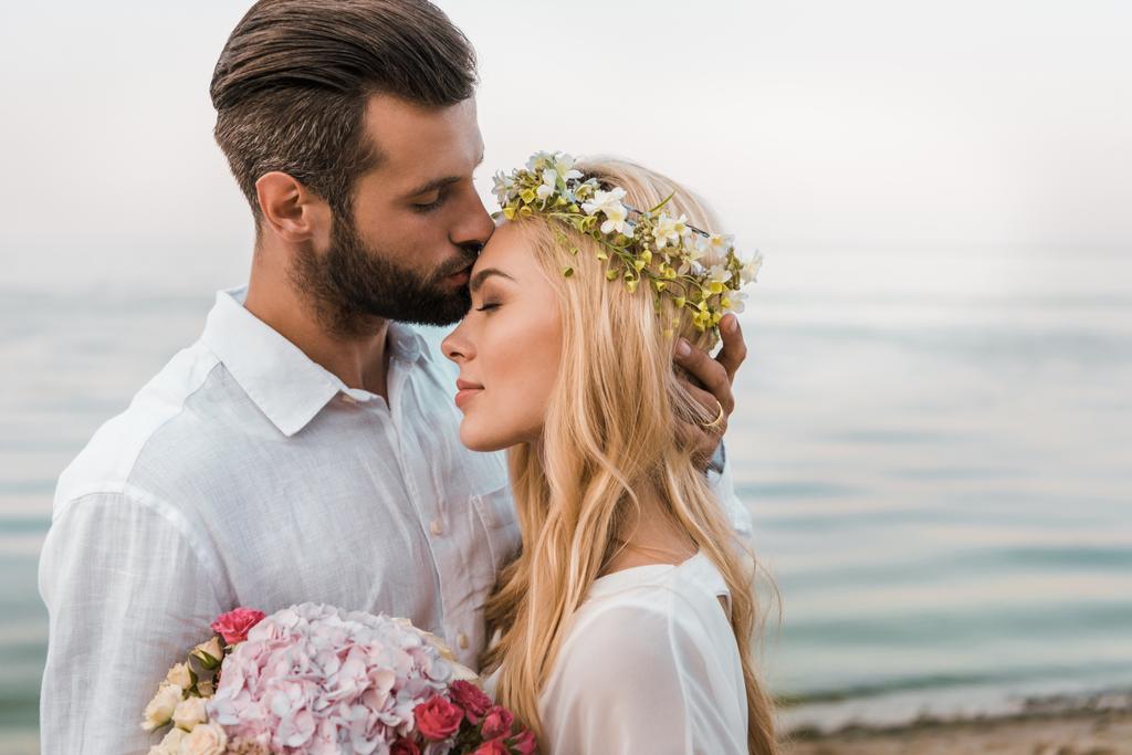 vue latérale du beau marié embrassant beau front de mariée sur la plage
 - Photo, image