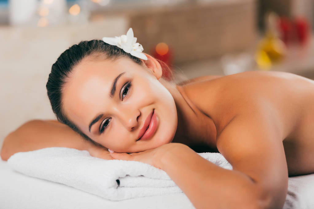 femme heureuse avec fleur dans les cheveux relaxant au salon de spa et en regardant la caméra
 - Photo, image