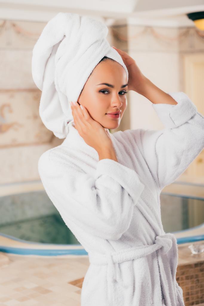joven mujer sonriente relajante con toalla en la cabeza en el centro de spa con piscina
 - Foto, imagen