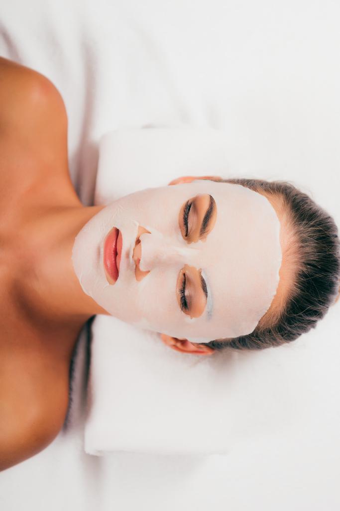 привлекательная молодая женщина в маске на лице расслабляющая с закрытыми глазами в спа-центре
 - Фото, изображение