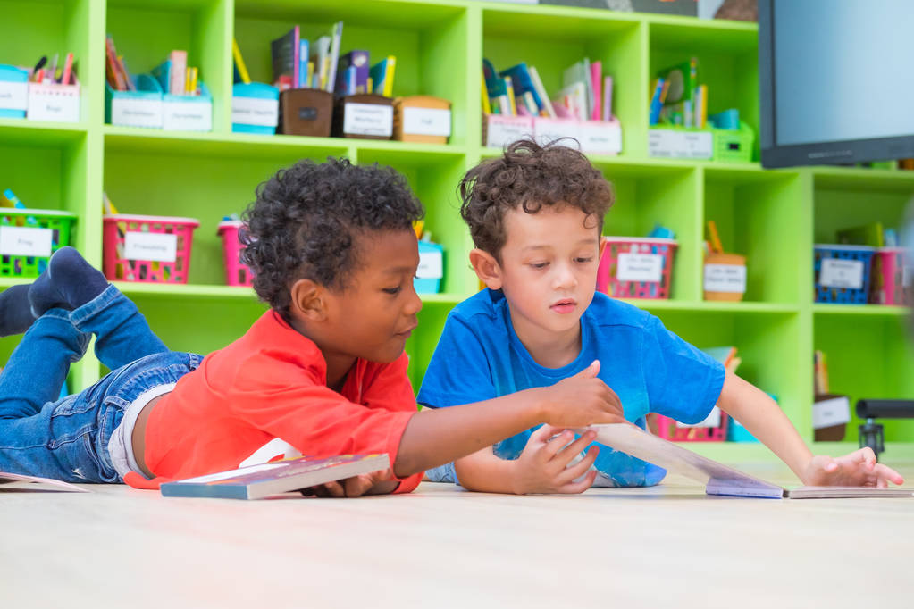Deux garçons s'allongent sur le sol et lisent un livre de contes dans une bibliothèque préscolaire, concept d'éducation à l'école maternelle
 - Photo, image