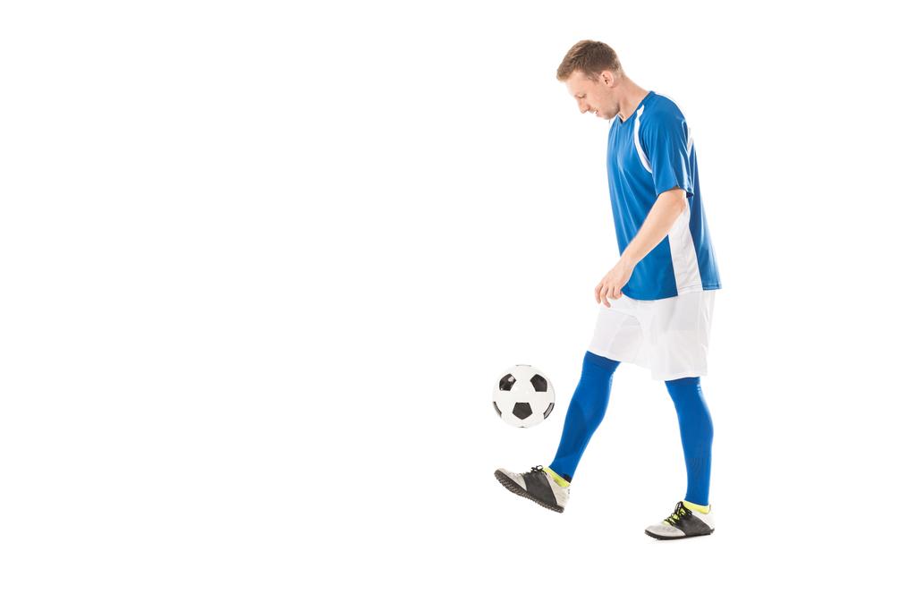 Zijaanzicht van de jonge voetballer bal schoppen en kijkt neer op geïsoleerde Wit - Foto, afbeelding
