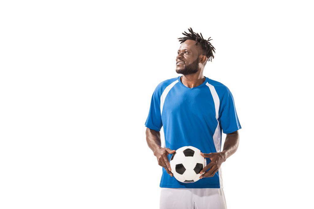 lächelnder afrikanisch-amerikanischer Sportler, der Fußball hält und isoliert auf weißem Grund wegschaut - Foto, Bild