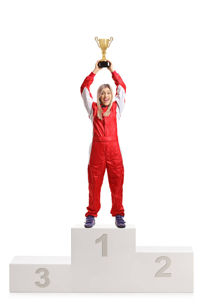 白い背景に分離された金のトロフィー カップ受賞者の台座の上の勝利を祝って幸せ女性レーサー - 写真・画像
